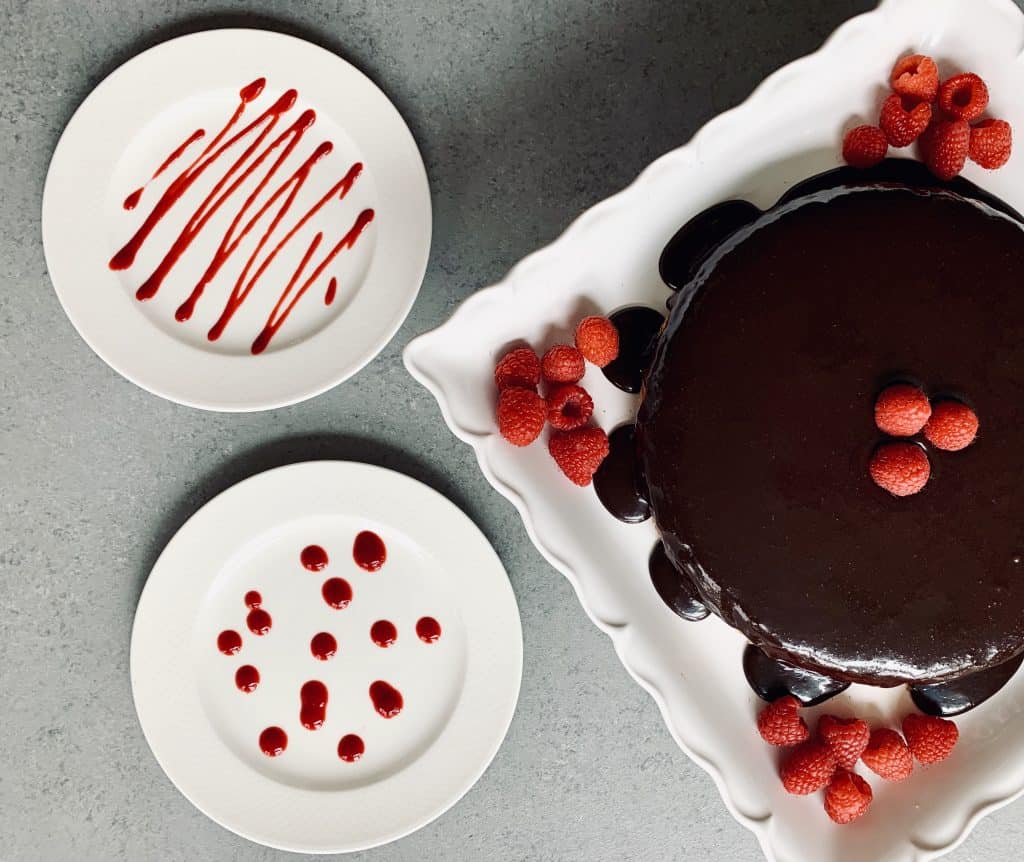 Plates decorated with raspberry coulis next to almond torte with chocolate nut butter icing