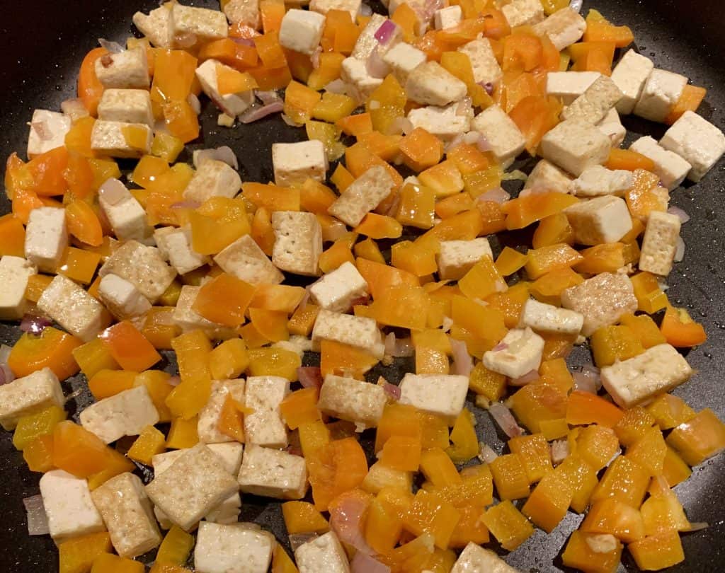 Tofu, yellow peppers, shallots and mango being heated in a non stick pan