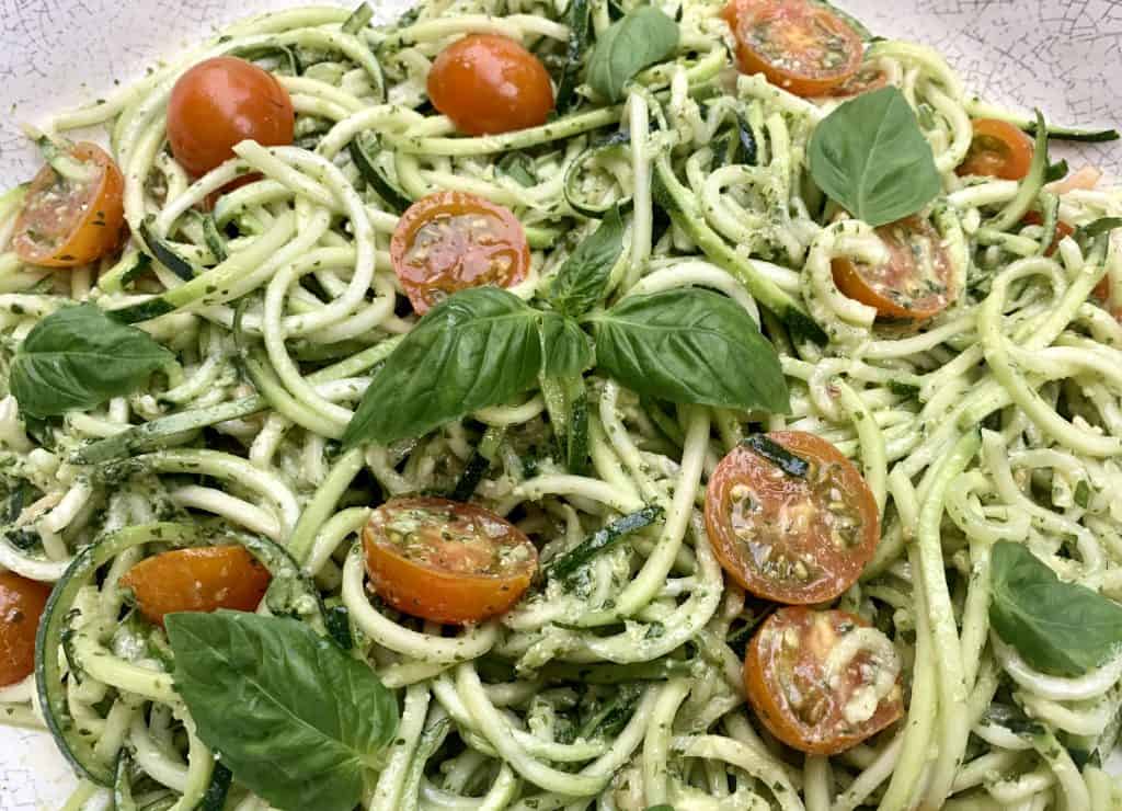 Pesto Zoodles and Tomato Salad pictured in a large serving bowl blended and topped with fresh basil leaves