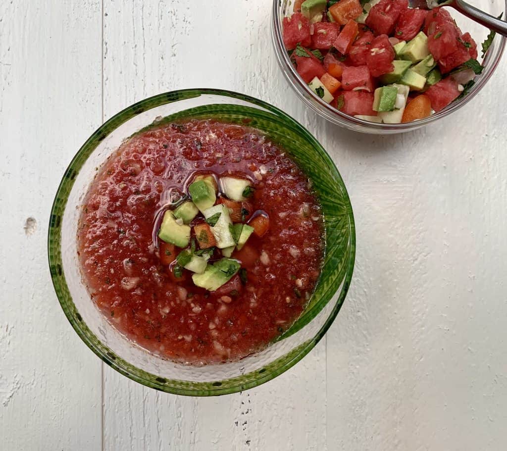 A bowl watermelon gazpacho with toppings in a separate bowl on the side
