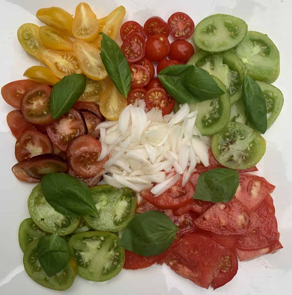 Garden tomatoes cut up an separated on a platter with cipollini onions and basil