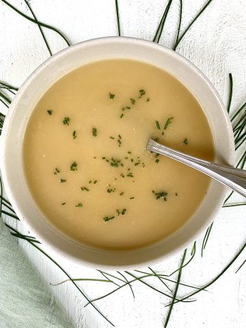 Vichyssoise Soup made with Potatoes, Cucumbers & Chives pictured in a bowl with scattered chives and a green napkin placed on a white wood board
