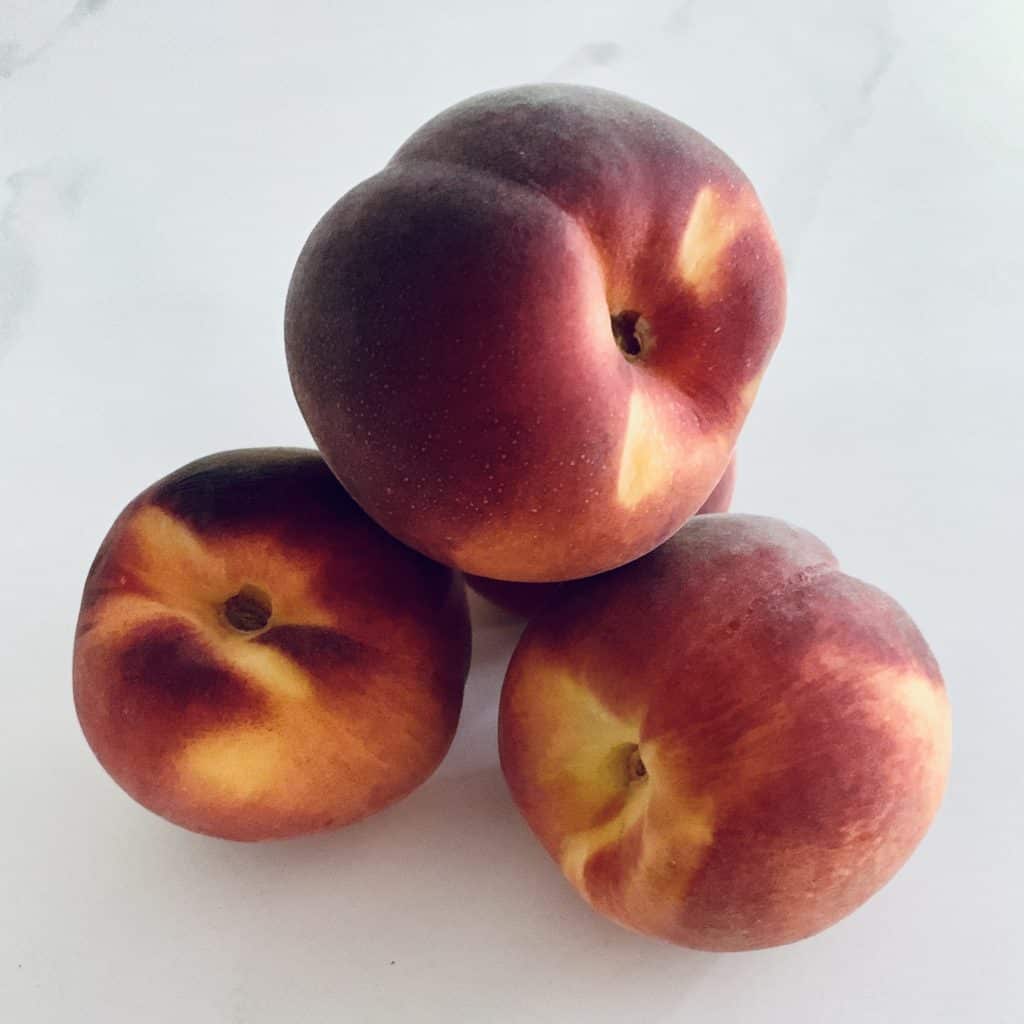 4 fresh whole peaches on a white table, leaning against each other 