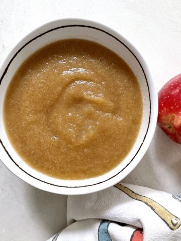 A bowl of homemade applesauce with an apple to the side