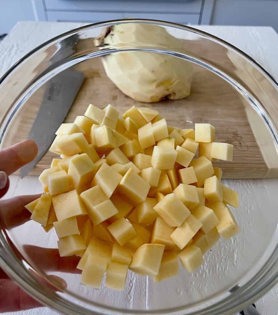 Cubed rutabaga in a glass bowl with a peeled rutabaga in the background on a cutting board