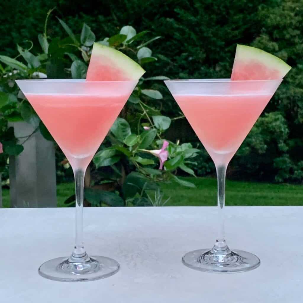 Two summer watermelon cosmo cocktails in chilled martini glasses, each with a watermelon wedge.