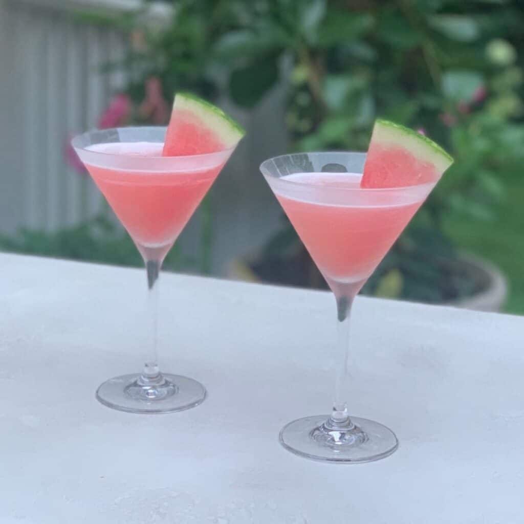 Blended watermelon cocktails in chilled martini glasses on a white tabletop outdoors.
